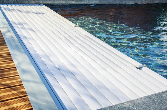 Extérieur piscine avec volet roulant automatique blanc semi-déployé sur bassin aux reflets bleus