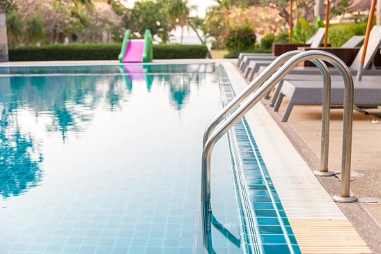 Piscine extérieure résidentielle avec margelles en pierre claire, escalier d'accès intégré et main courante en acier inoxydable