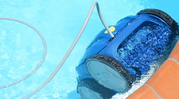 Robot nettoyeur automatique de piscine en fonctionnement dans bassin résidentiel avec margelles en béton teinté orange